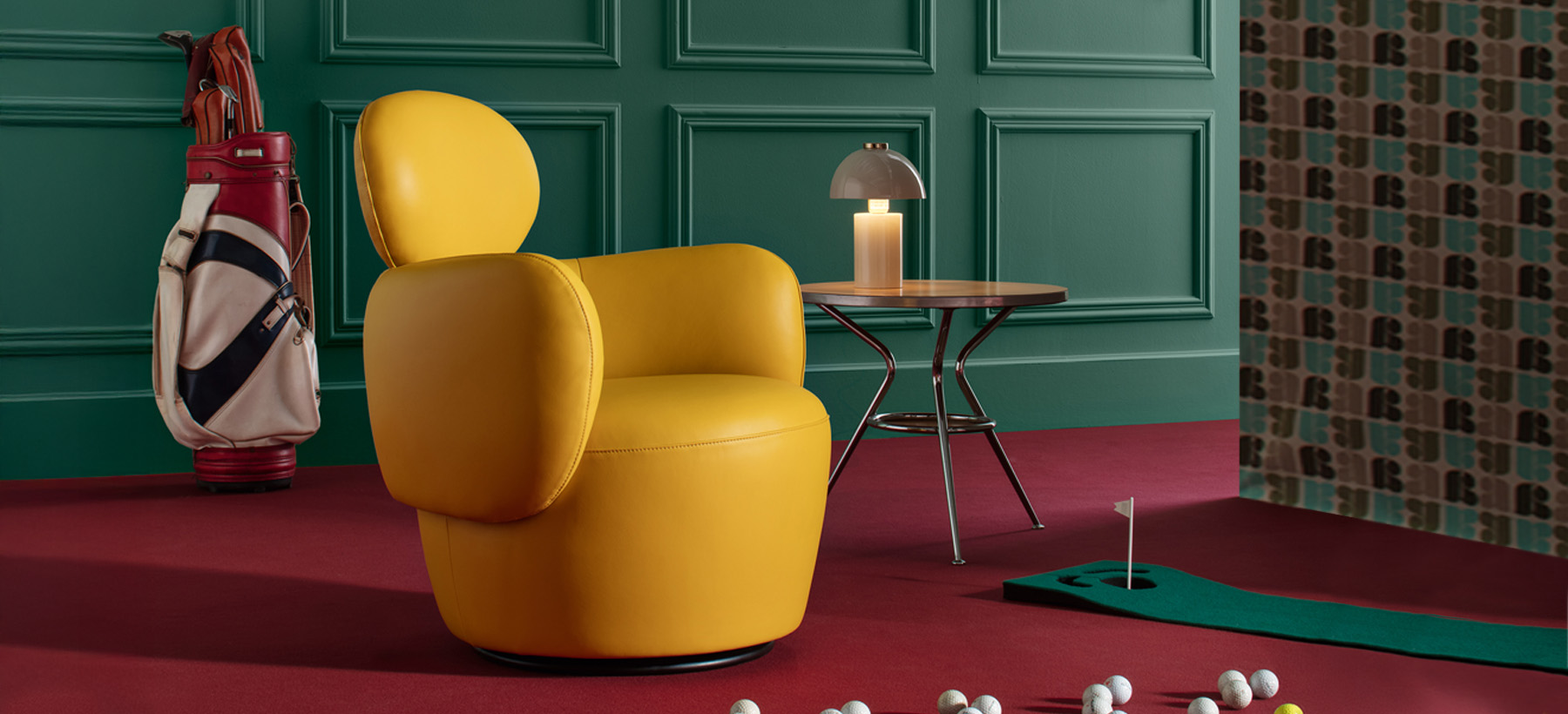 Yellow armchair with rounded design placed on a red carpet, in front of a green paneled wall, with a designer lamp and golf balls scattered on the floor.