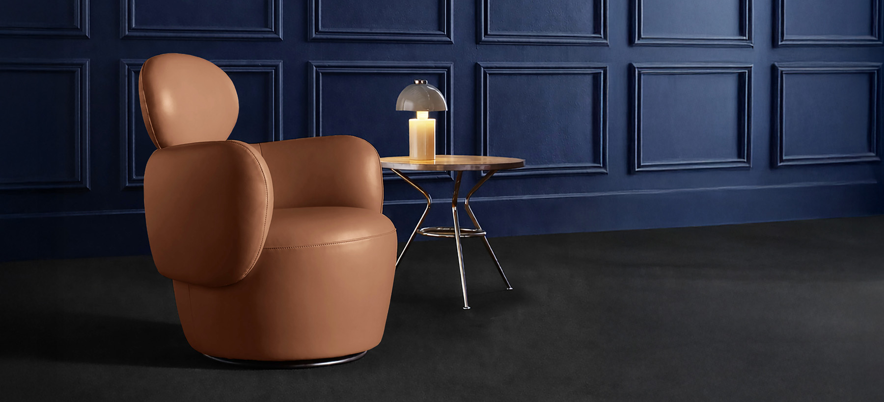 Beige fabric armchair with rounded shapes, placed on a soft pink floor against a burgundy wall, in a minimalist and elegant setting.