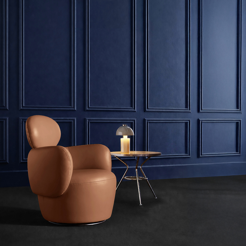 Beige fabric armchair with rounded shapes, placed on a soft pink floor against a burgundy wall, in a minimalist and elegant setting.