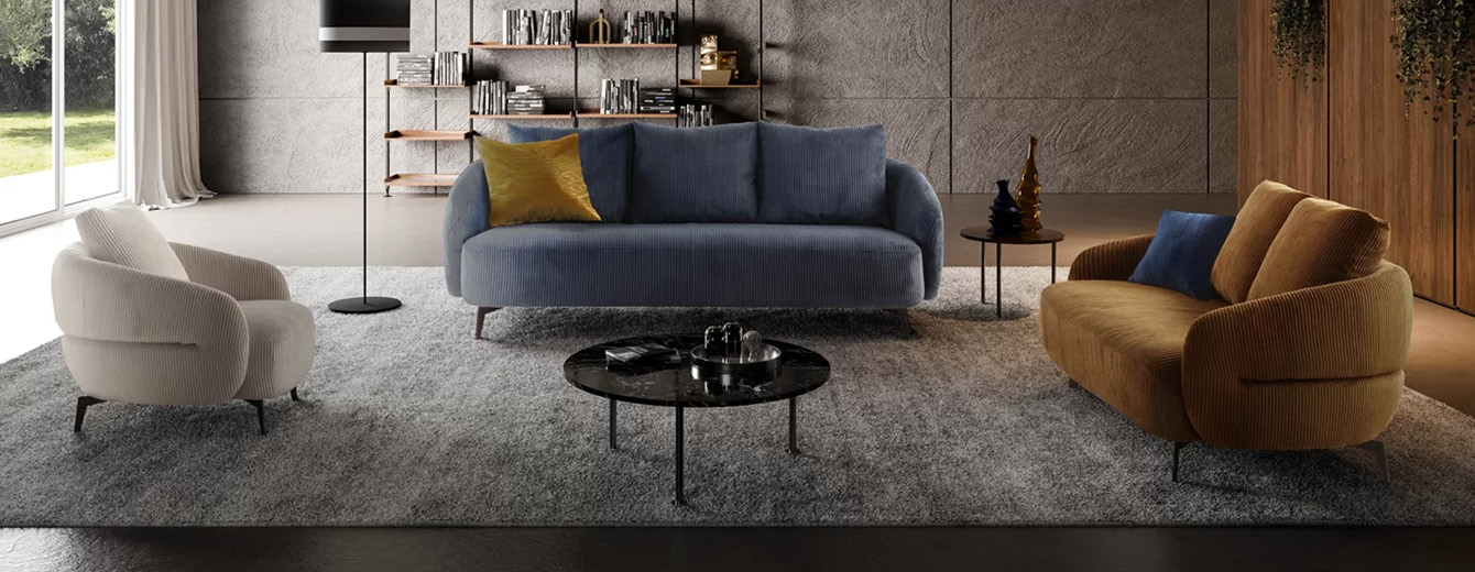 Salon moderne avec un canapé bleu en velours côtelé, une banquette jaune moutarde et un fauteuil crème, disposés sur un tapis gris avec une décoration minimaliste et une bibliothèque murale.