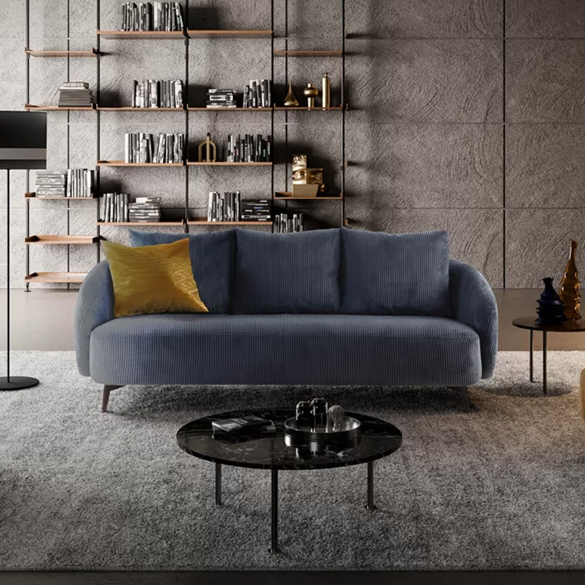 Salon moderne avec un canapé bleu en velours côtelé, une banquette jaune moutarde et un fauteuil crème, disposés sur un tapis gris avec une décoration minimaliste et une bibliothèque murale.