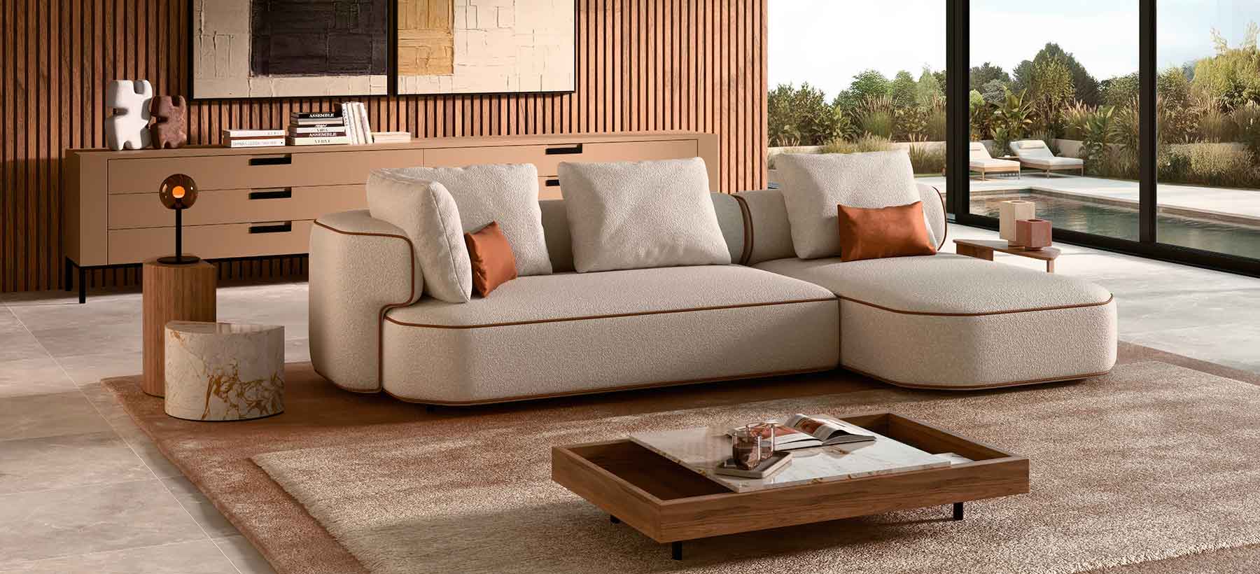Curved contemporary sectional sofa upholstered in textured off-white fabric with warm leather piping, set in a modern living room featuring wooden slat walls, abstract art, and large floor-to-ceiling windows opening onto a landscaped terrace.