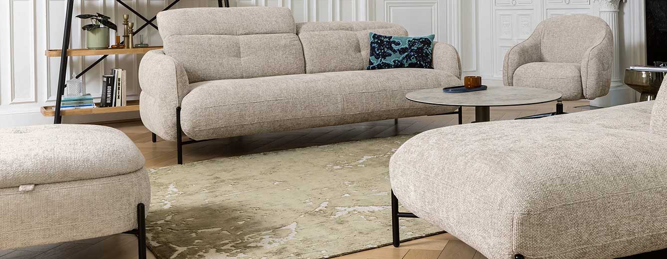 Compact sofa upholstered in beige textured fabric, featuring a rounded silhouette, adjustable headrests, and a black metal base.