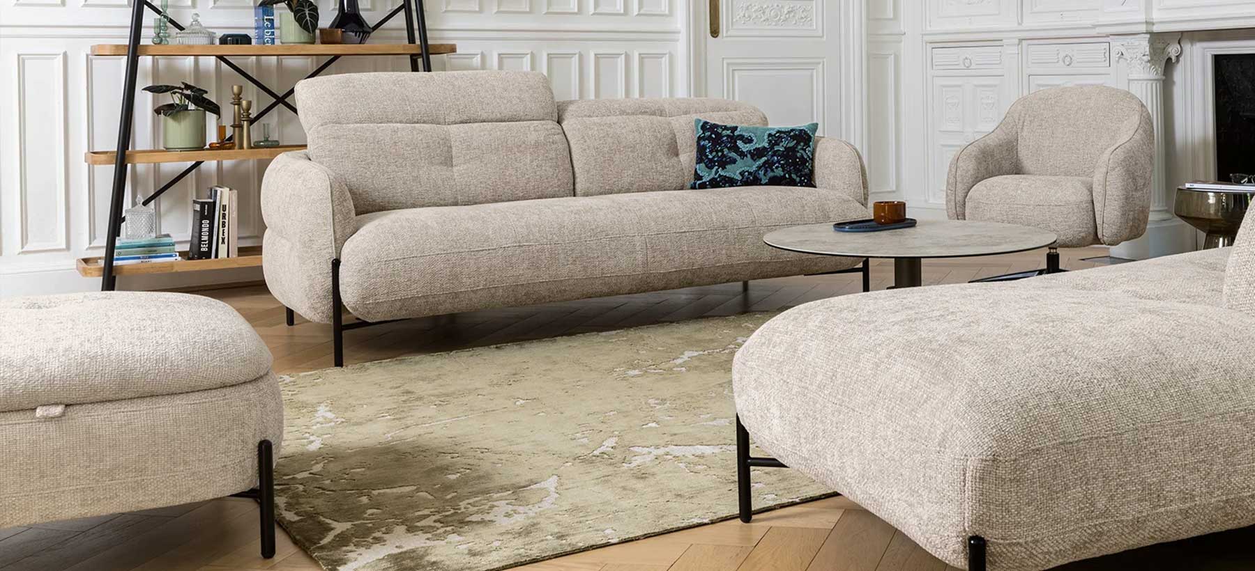 Canapé compact en tissu texturé beige, silhouette arrondie, têtières relevables et piètement métallique noir.