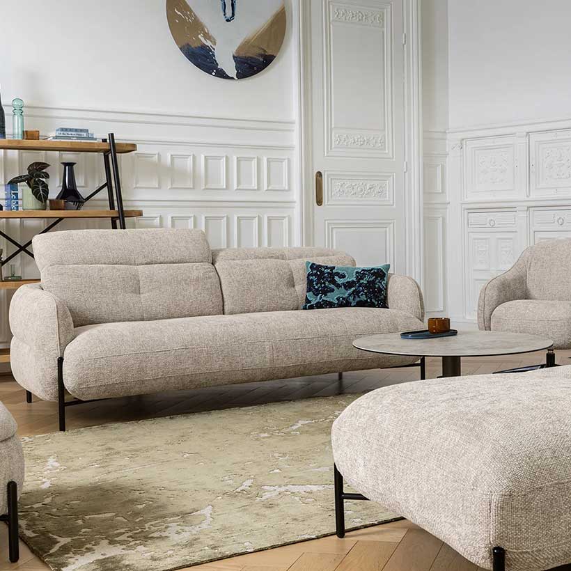Compact sofa upholstered in beige textured fabric, featuring a rounded silhouette, adjustable headrests, and a black metal base.