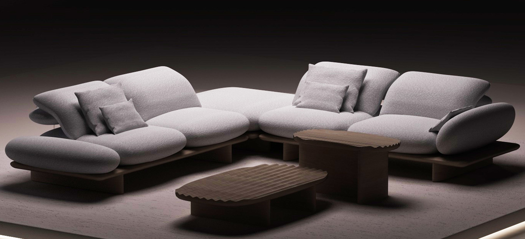 Canapé d’angle design gris clair aux formes organiques, accompagné de tables basses en bois sur une plateforme éclairée, dans une ambiance minimaliste et contemporaine.