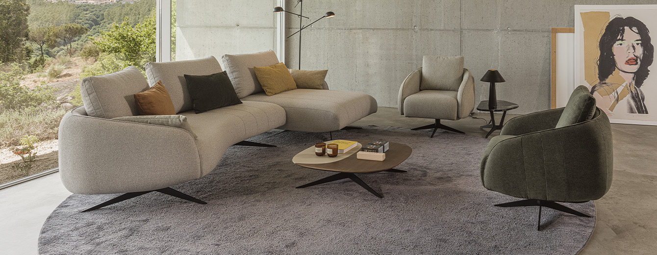 Sculptural sofa with an elongated silhouette, textured beige upholstery, recessed slim legs, and organic lines inspired by pebbles.