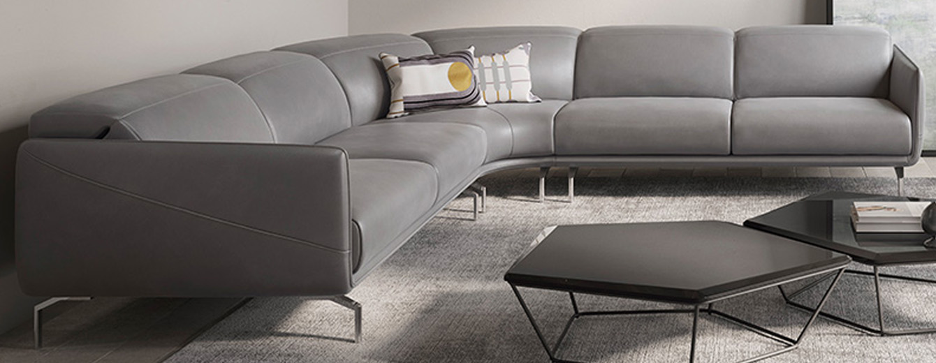 Canapé d’angle design en cuir gris avec piètement métallique fin, lignes épurées et assise spacieuse, dans un salon contemporain.