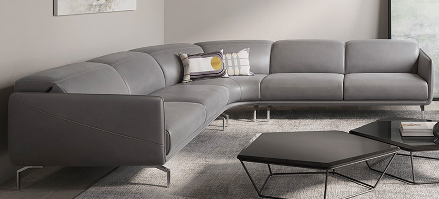 Canapé d’angle design en cuir gris avec piètement métallique fin, lignes épurées et assise spacieuse, dans un salon contemporain.