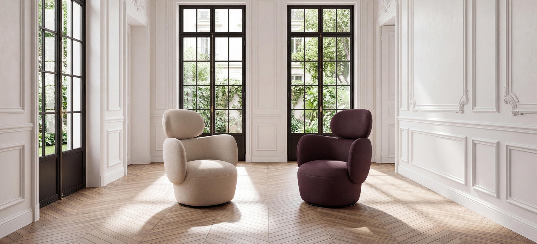 Two fabric armchairs with rounded shapes, one beige and one burgundy, set on a herringbone parquet floor in a bright Parisian interior with white moldings and large windows overlooking lush greenery.